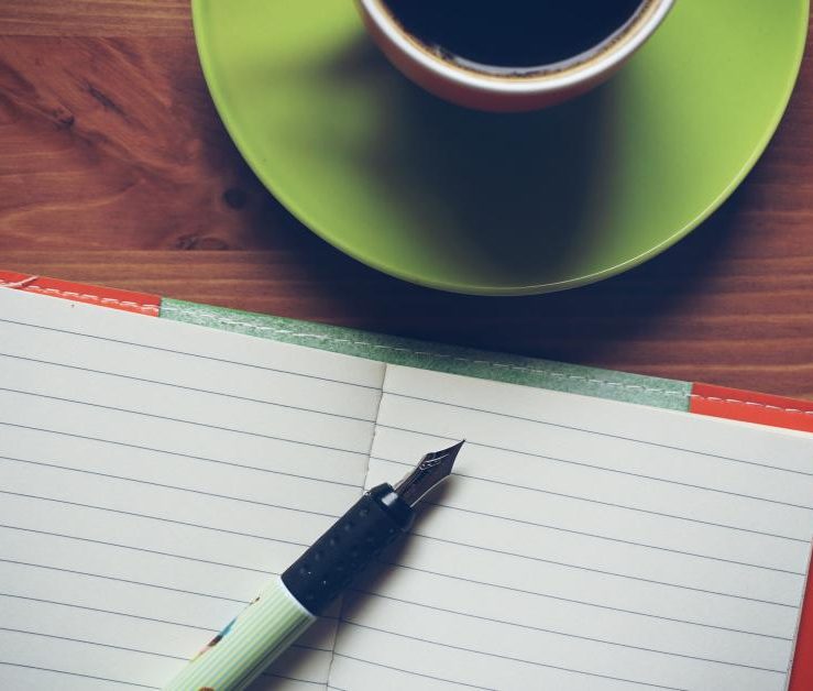 A notebook and pen beside a green cup on a desk, seen from above